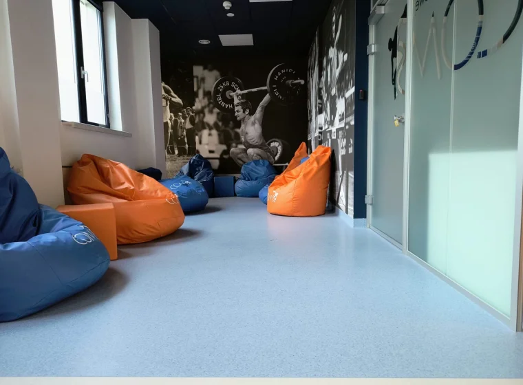 Korytarz i sala relaksu w Centalnym Ośrodku Medycyny Sportowej, błękitna wykładzina Tarkett IQ Granit, pufy niebieskie i pomarańczowe