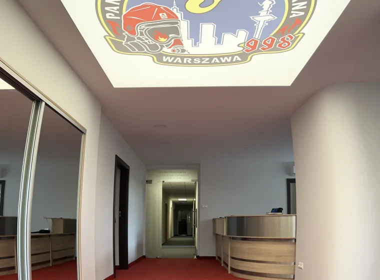 Korytarz w Państwowej Straży Pożarnej w Warszawie, czerwona elegancka jednolita wykładzina dywanowa oraz logo na suficie